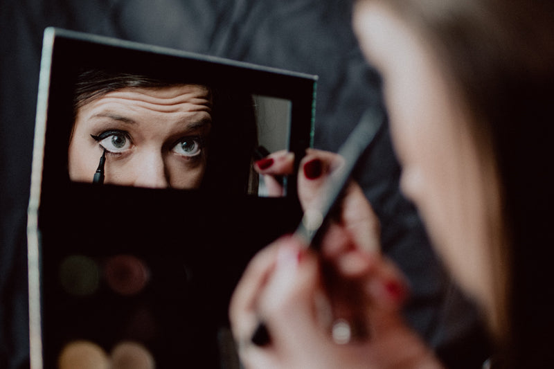A woman applying black eyeliner in a compact mirror