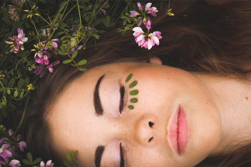 Woman lay in grass and flowers with glowing skin that is a result of cleansing and toning your face