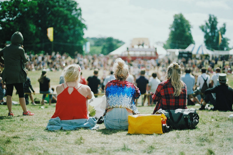 demonstrating festival tips for first timers, three women are sitting on grass overlooking the crowd. 