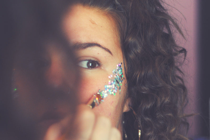 Girl applying glitter to her face, which is on the the must have festival beauty products 
